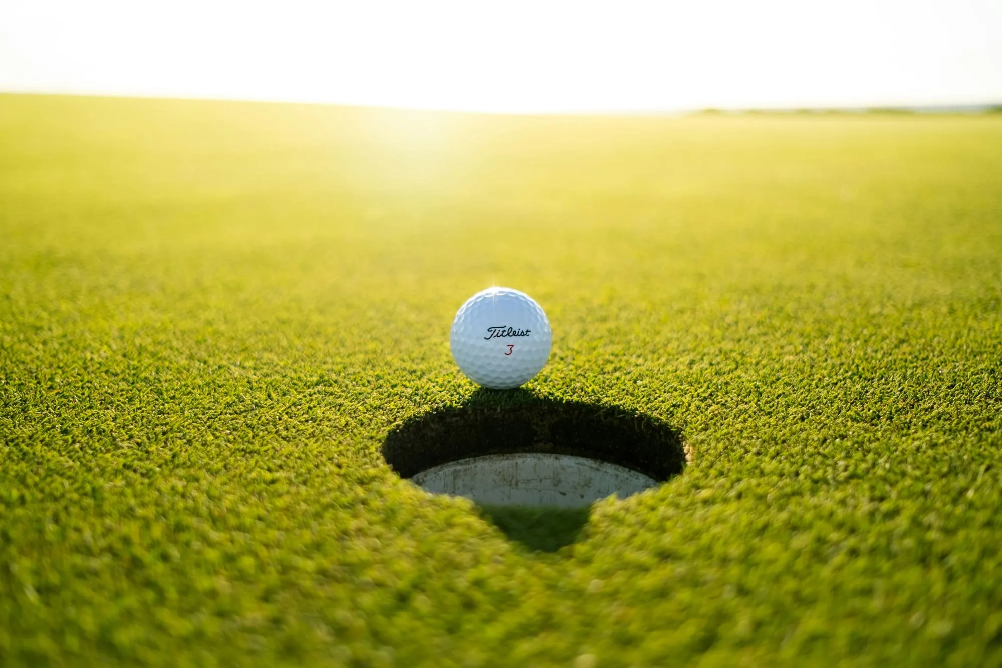 A golf ball resting on the lip of the cup