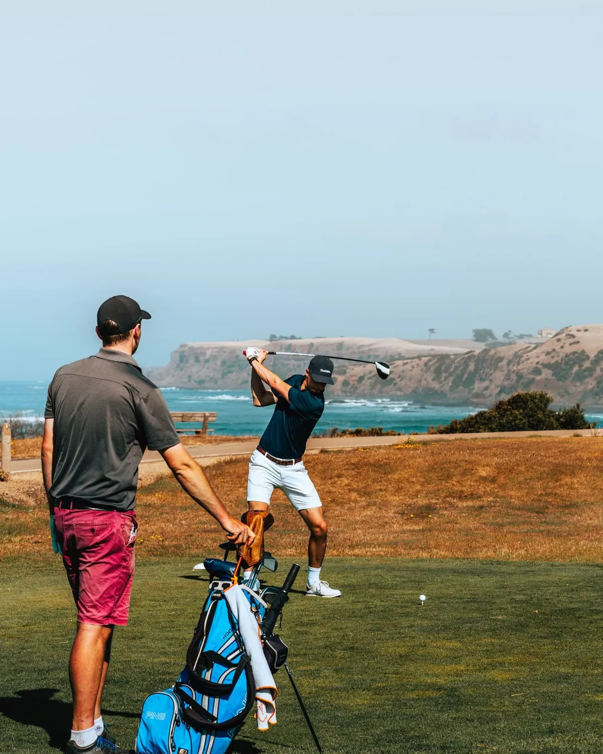 Two golfers on a tee by the ocean